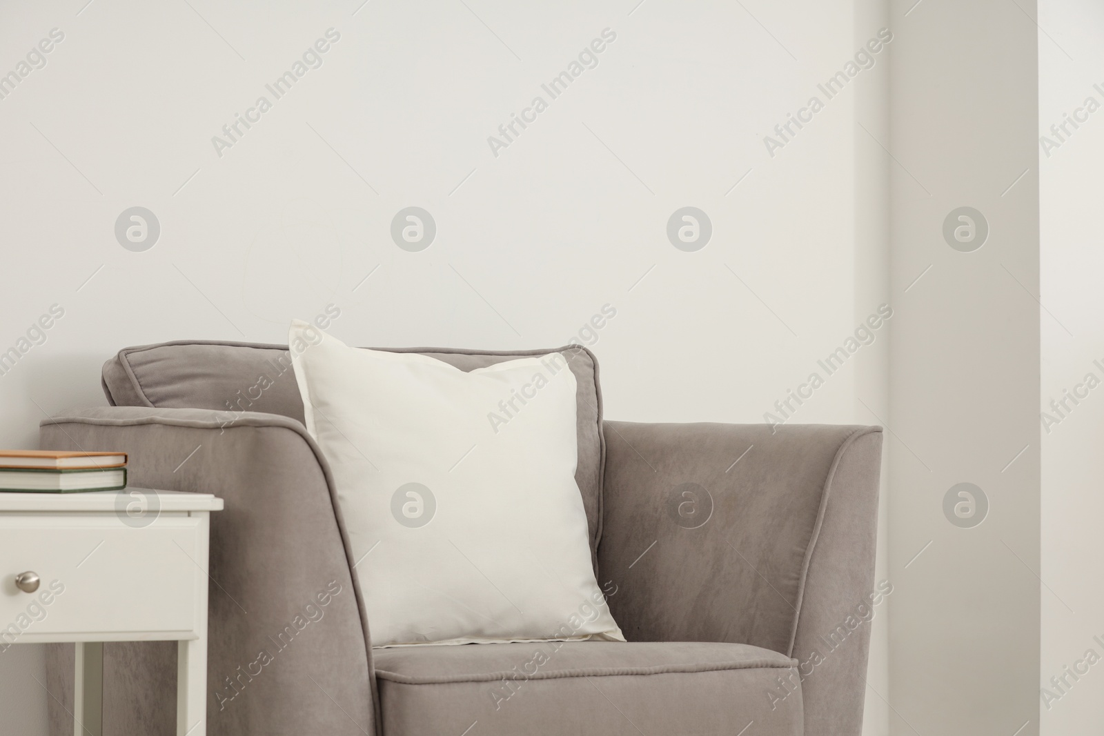 Photo of Soft white pillow on armchair and bedside table near light wall indoors