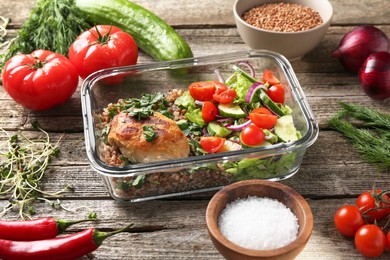 Photo of Healthy meal. Cutlet, buckwheat and salad in container near other products on wooden table