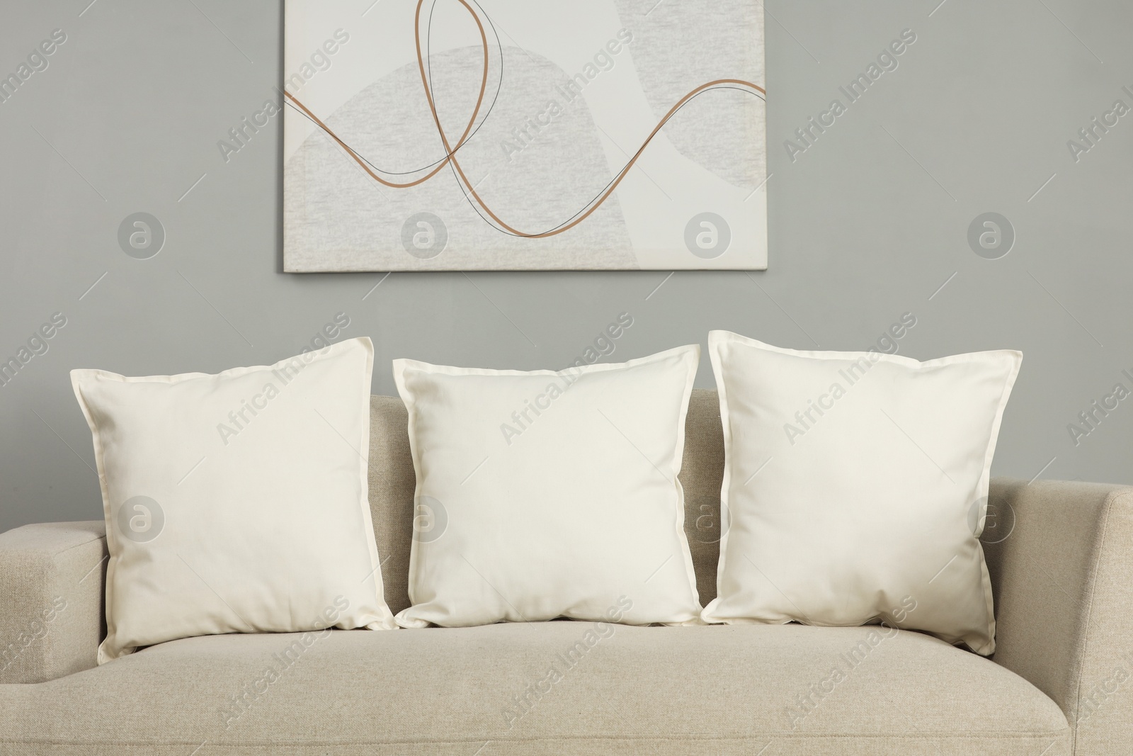 Photo of Soft white pillows on sofa near grey wall indoors