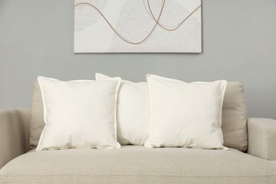 Photo of Soft white pillows on sofa near grey wall indoors