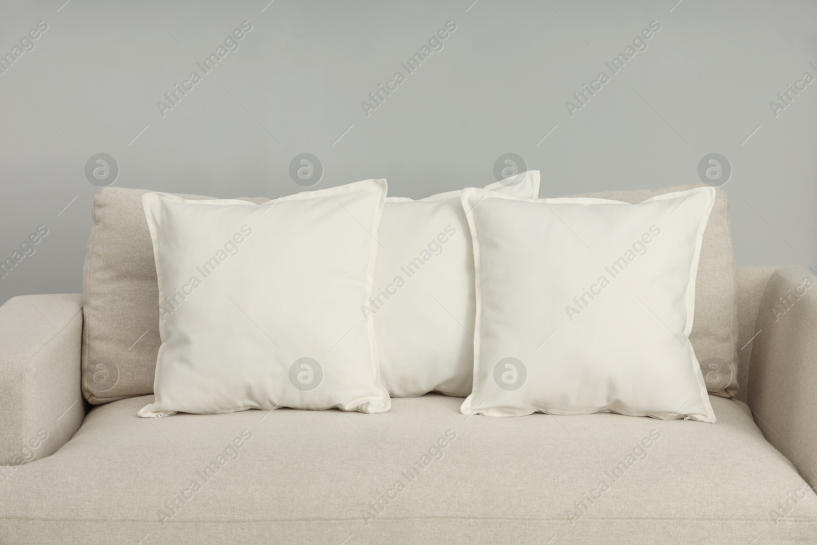 Photo of Soft white pillows on sofa near grey wall indoors