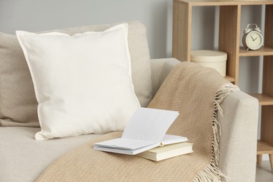 Photo of Soft white pillow, blanket and books on sofa indoors