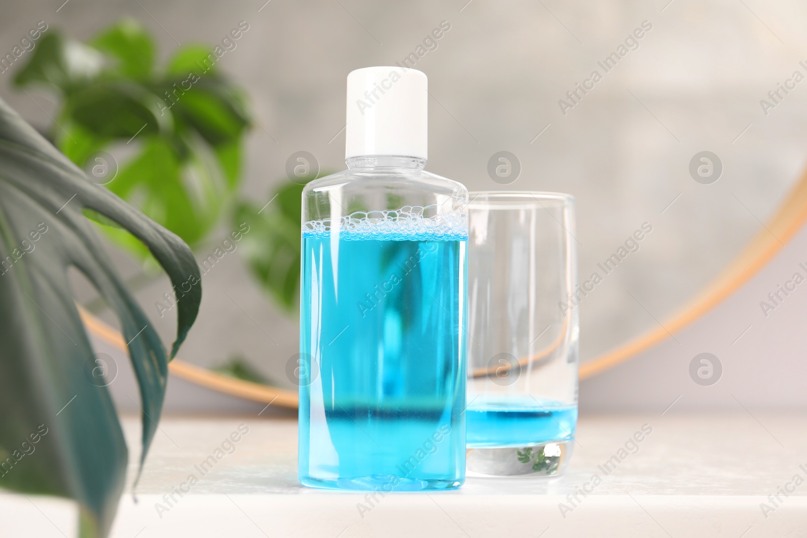 Photo of Bottle of mouthwash and glass on white table in bathroom