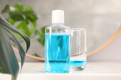 Photo of Bottle of mouthwash and glass on white table in bathroom