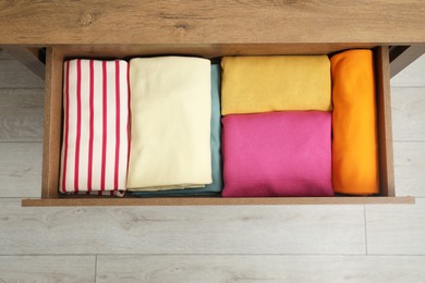 Wooden chest of drawers with different folded clothes indoors, top view