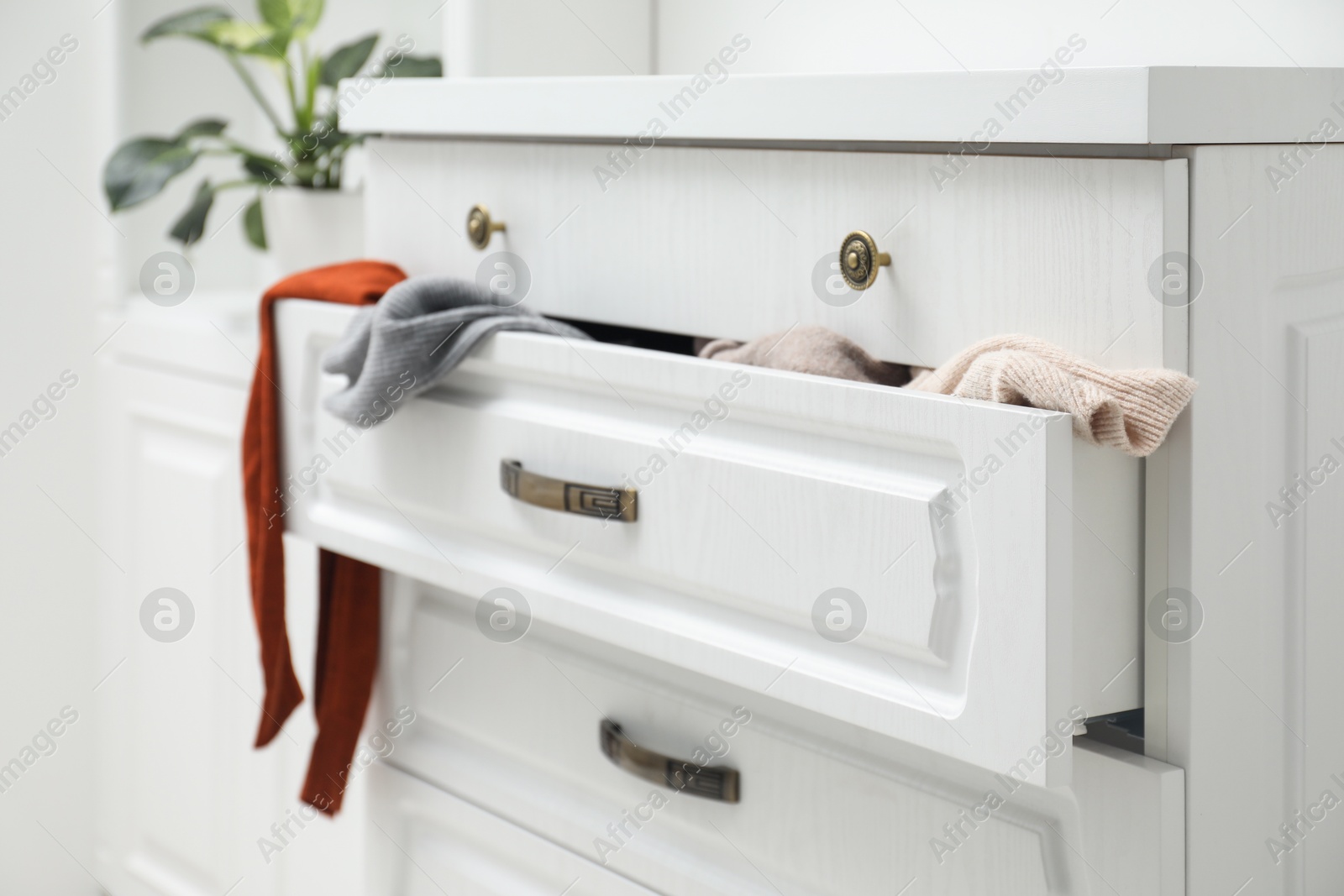 Photo of Cluttered chest of drawers indoors. Clothes in mess