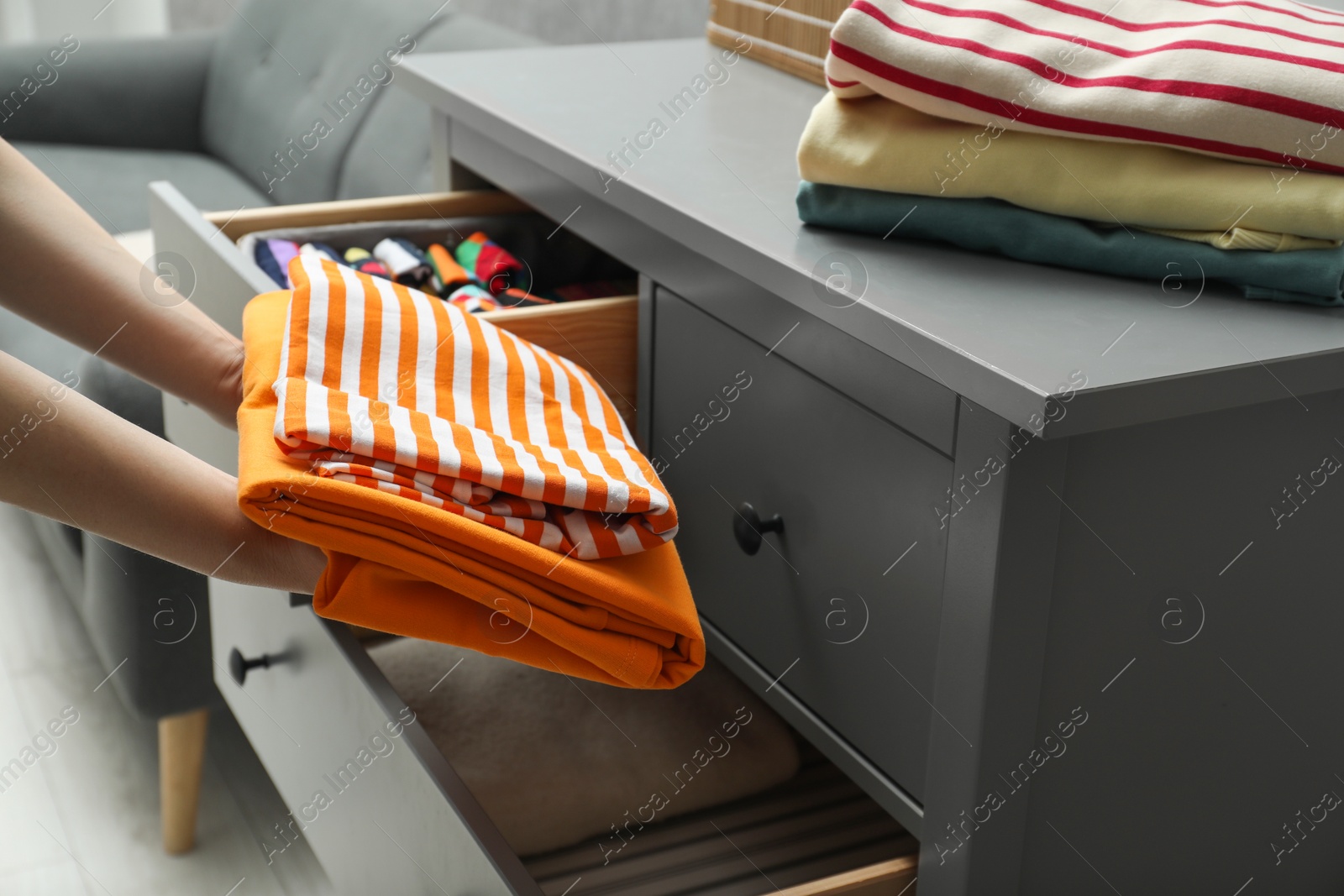 Photo of Woman putting folded clothes into drawer indoors, closeup