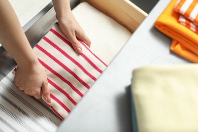 Photo of Woman putting folded clothes into drawer indoors, top view