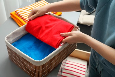 Woman putting folded clothes into storage basket indoors, closeup