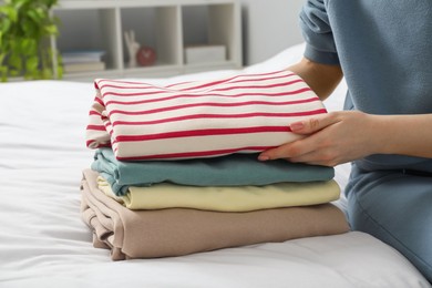 Woman folding clothes on bed indoors, closeup