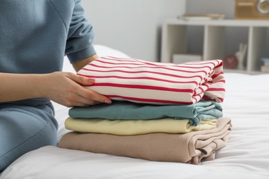 Woman folding clothes on bed indoors, closeup