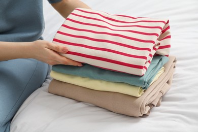 Woman folding clean clothes on bed, closeup