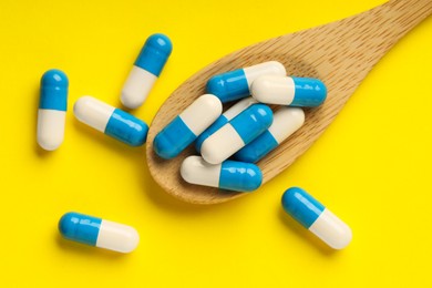 Photo of Antibiotic pills and spoon on yellow background, top view