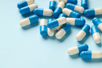 Many antibiotic pills on light blue background, closeup. Space for text