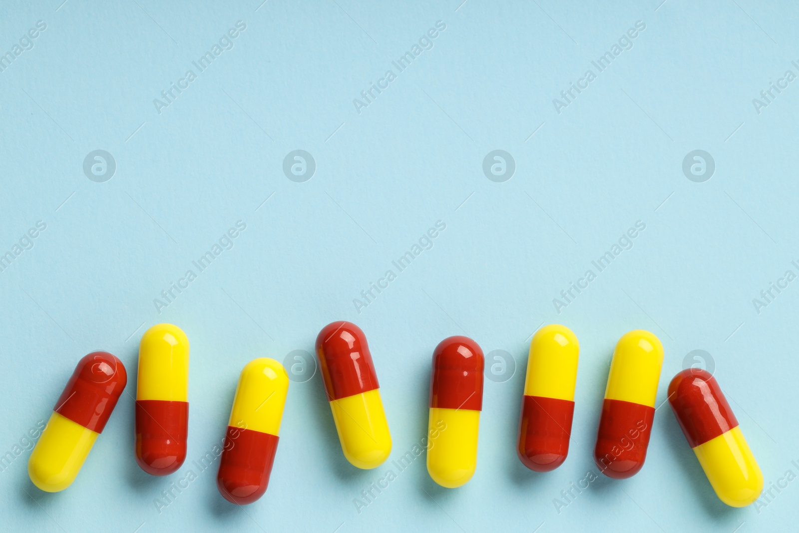 Photo of Many antibiotic pills on light blue background, top view. Space for text