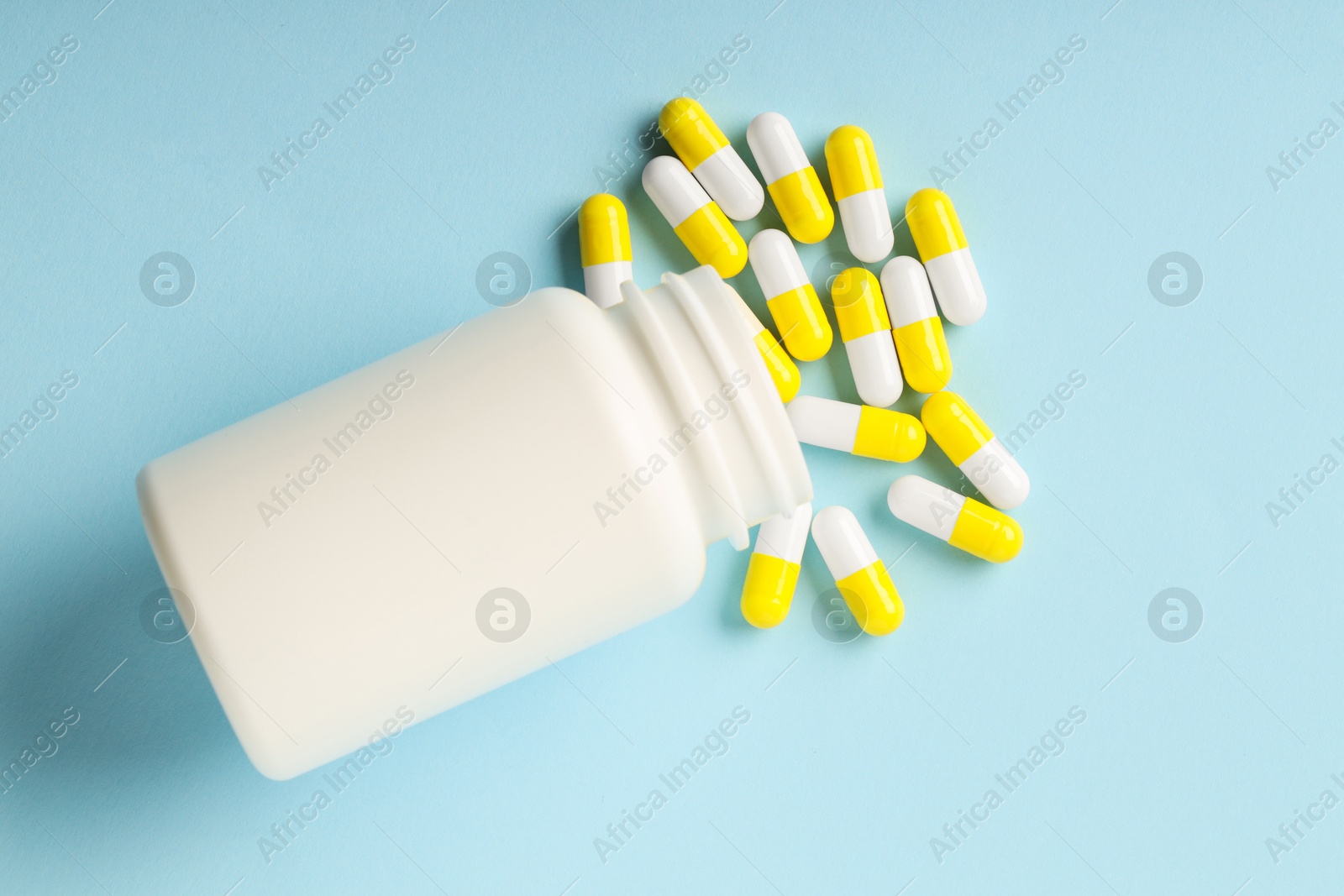 Photo of Antibiotic pills and bottle on light blue background, top view