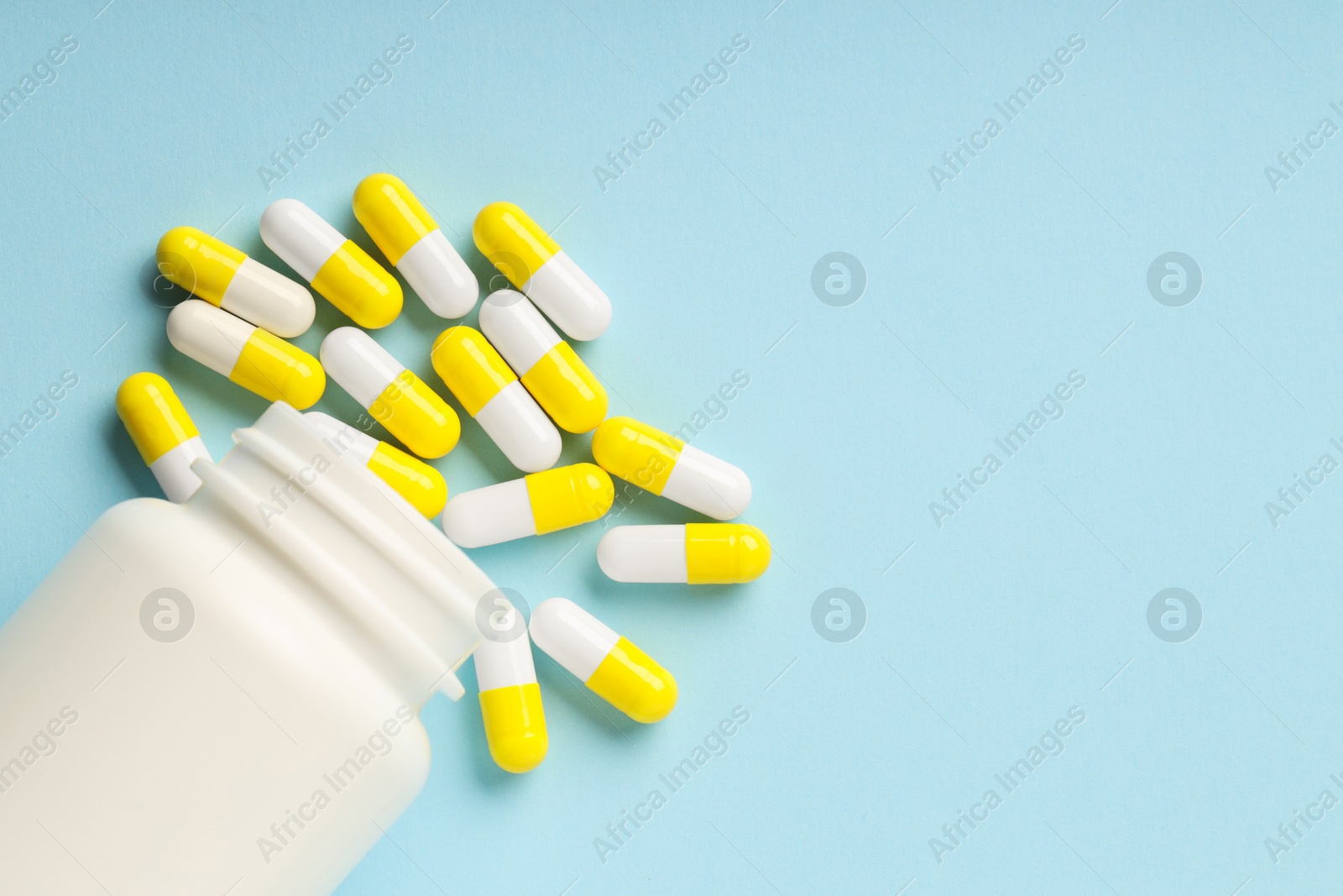 Photo of Antibiotic pills and bottle on light blue background, top view. Space for text