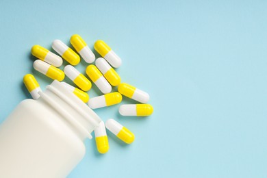 Antibiotic pills and bottle on light blue background, top view. Space for text