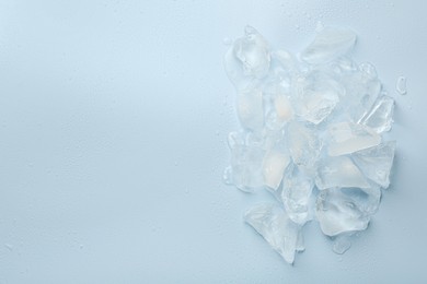 Pieces of crushed ice on light blue background, top view. Space for text