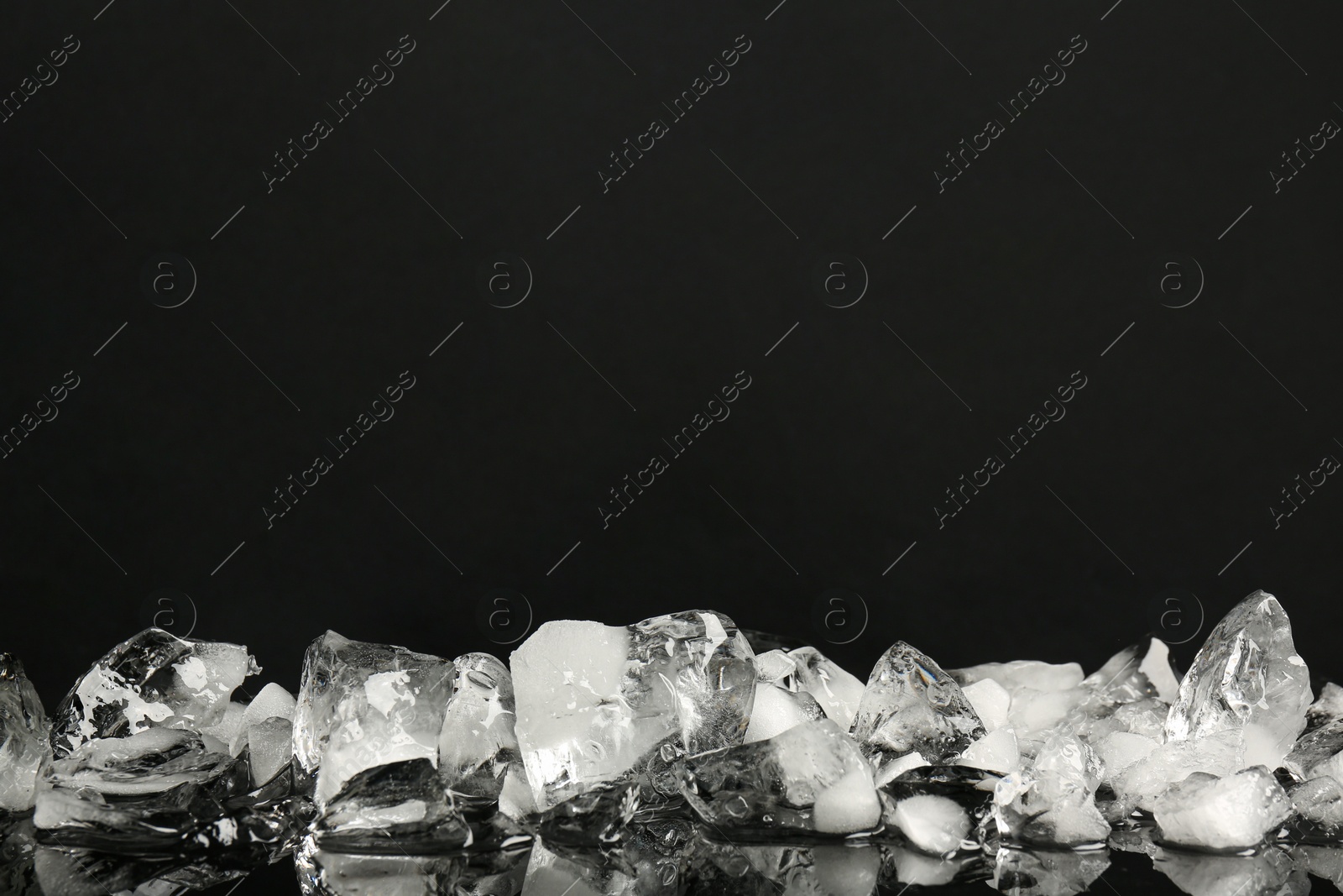 Photo of Pile of crushed ice on black mirror surface, space for text