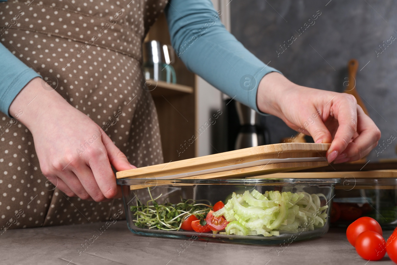 Photo of Healthy food. Woman closing glass container with fresh vegetables at grey table, closeup