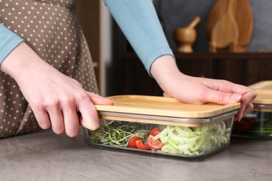 Photo of Healthy food. Woman closing glass container with fresh vegetables at grey table, closeup