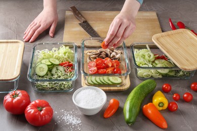 Healthy food. Woman putting piece of tomato into glass container at grey table, closeup