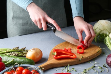 Photo of Healthy food. Woman cutting pepper at grey table, closeup