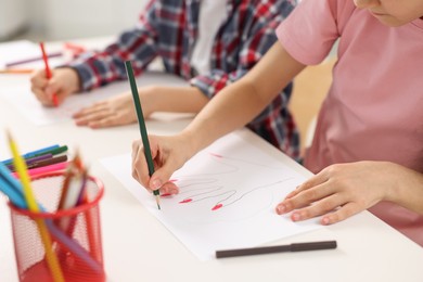 Photo of Brother and sister drawing at white table indoors, closeup