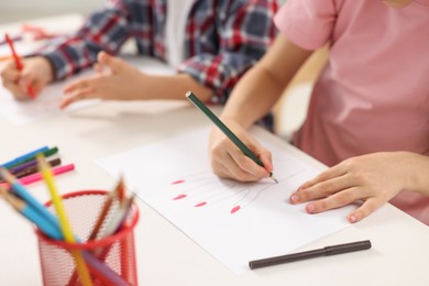 Photo of Brother and sister drawing at white table indoors, closeup