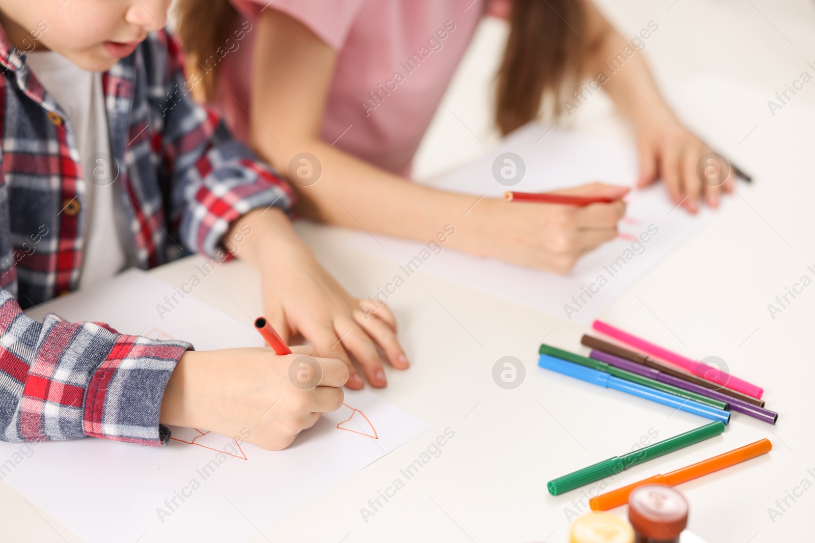 Photo of Brother and sister drawing at white table, closeup