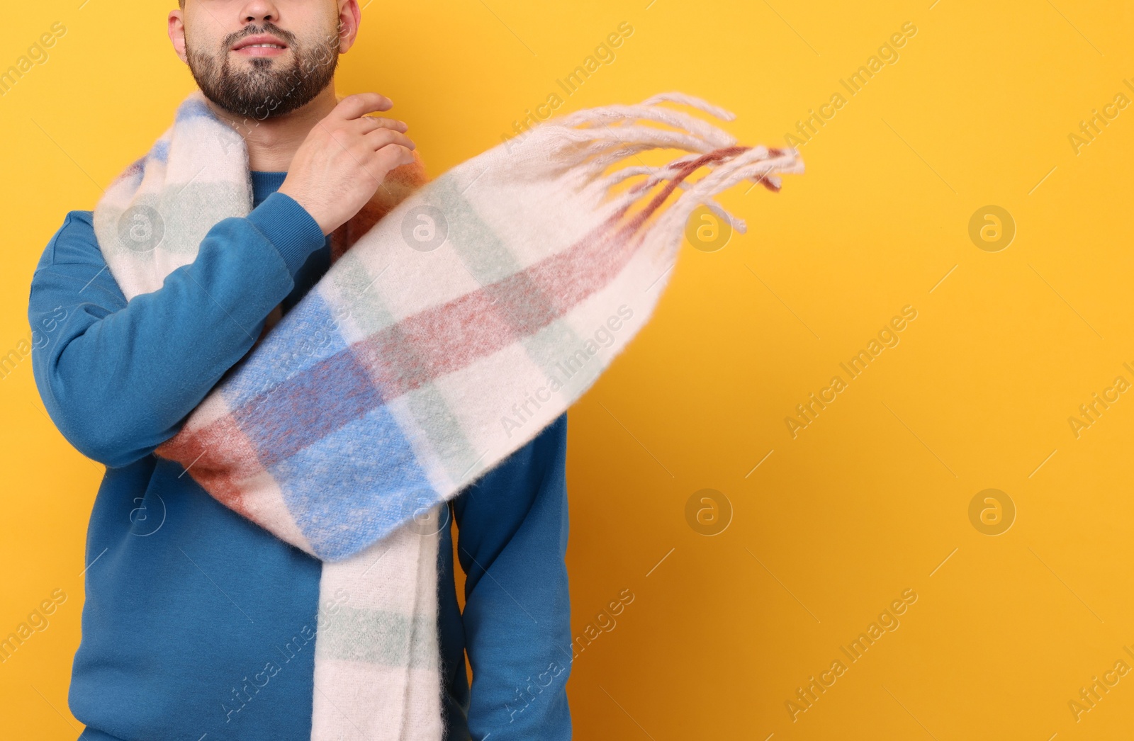Photo of Smiling man in warm scarf on yellow background, closeup. Space for text