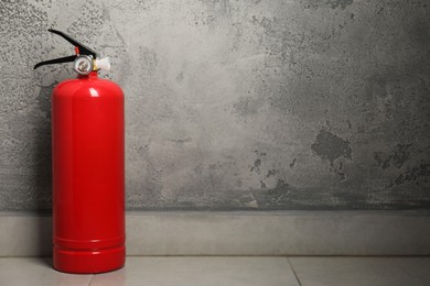 Photo of Fire extinguisher on floor near grey textured wall, space for text