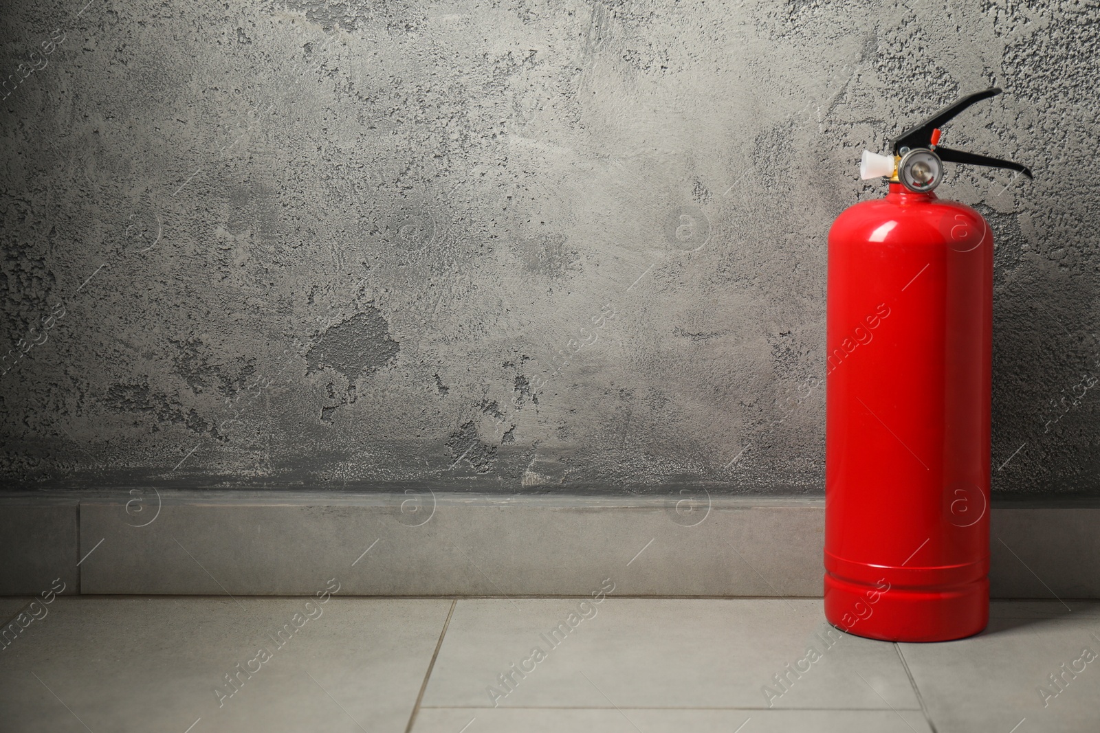 Photo of Fire extinguisher on floor near grey textured wall, space for text