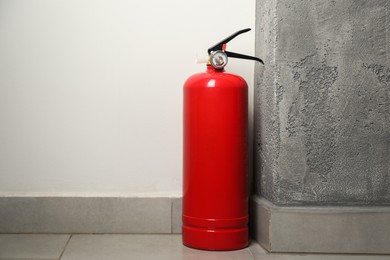 Fire extinguisher on floor near grey wall indoors