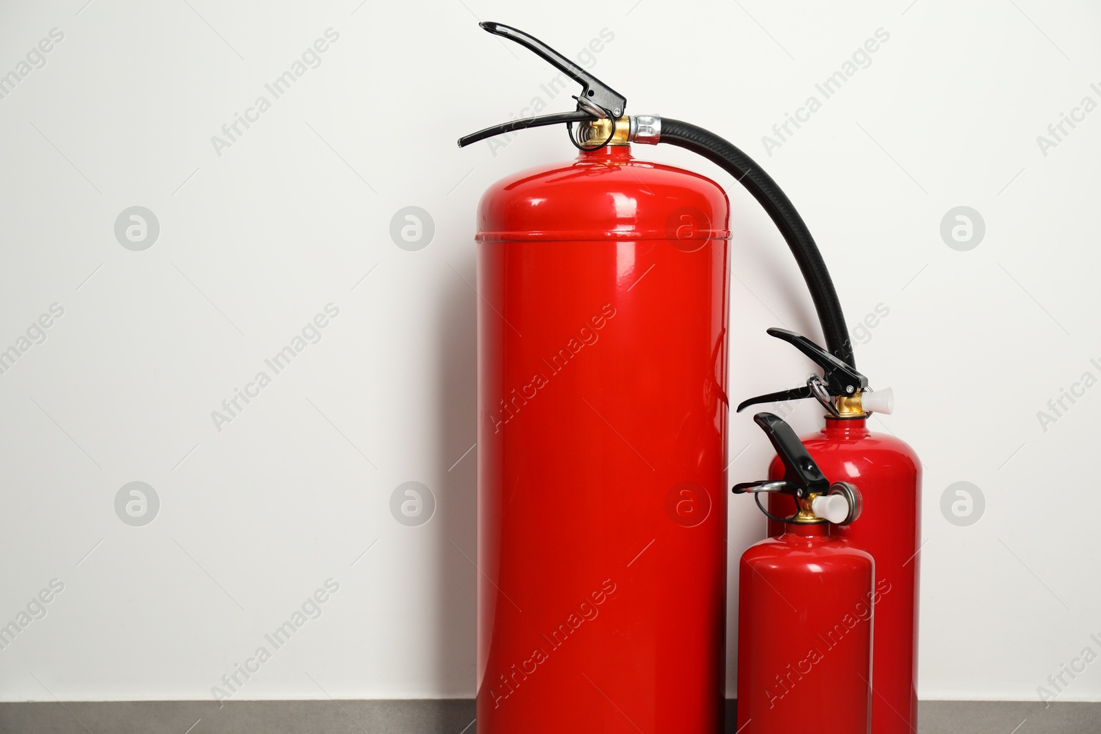 Photo of Three red fire extinguishers near light wall