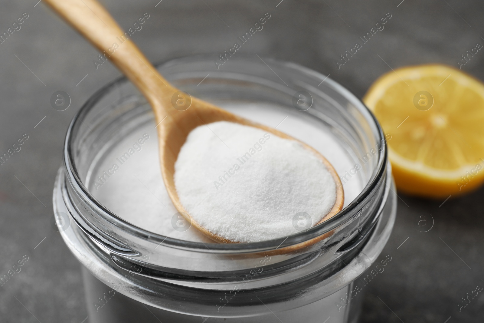 Photo of Baking soda, spoon and lemon on grey table, closeup