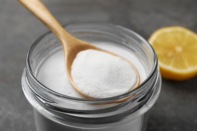 Baking soda, spoon and lemon on grey table, closeup