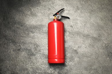 One red fire extinguisher on gray textured background, top view