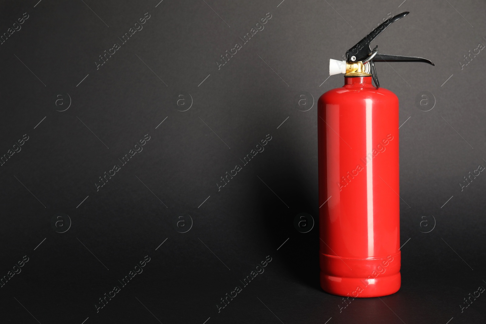 Photo of One red fire extinguisher on dark gray background, space for text