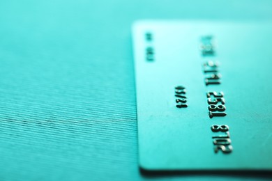 Photo of One credit card on turquoise background, closeup. Space for text