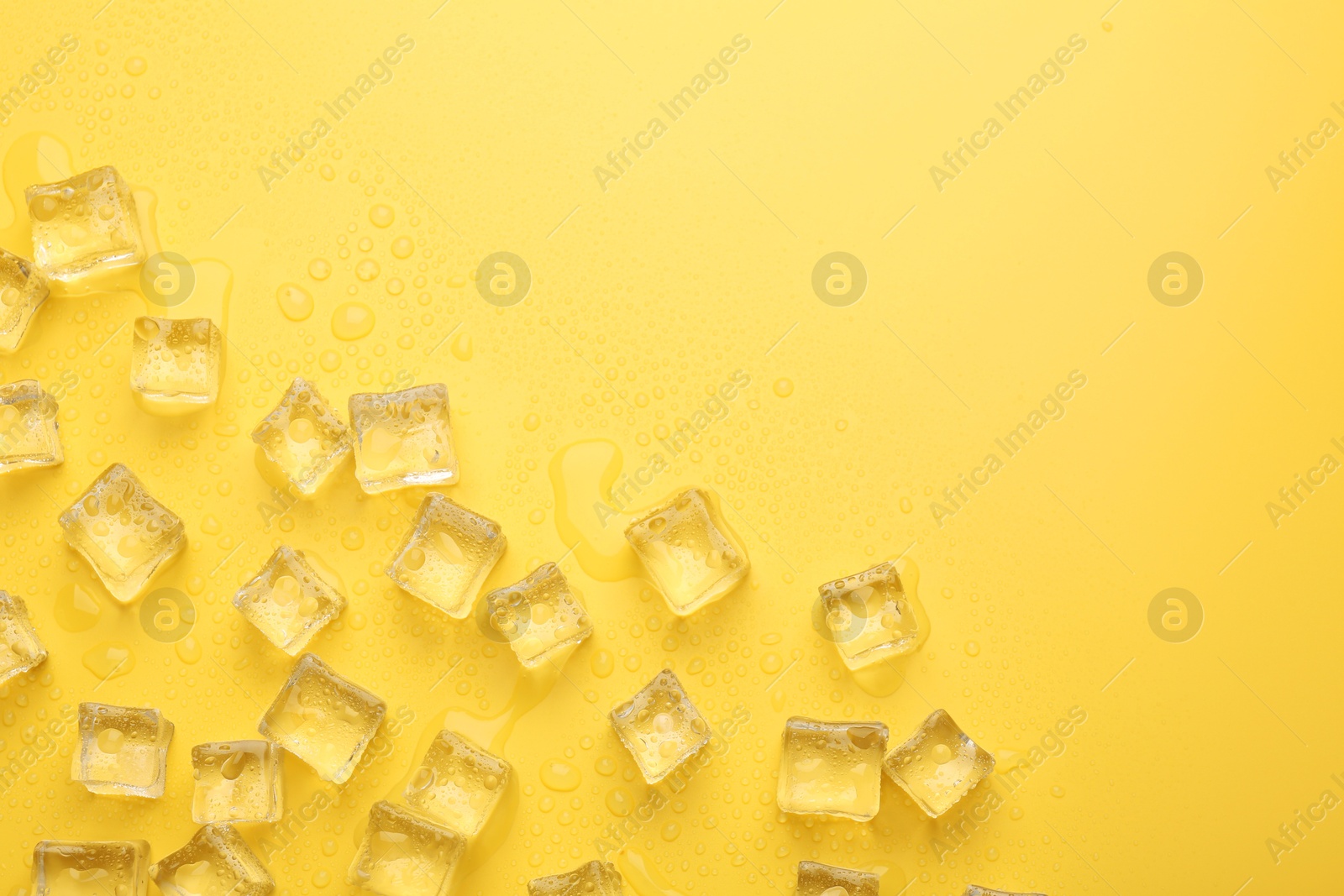 Photo of Crystal clear ice cubes on yellow background, flat lay. Space for text