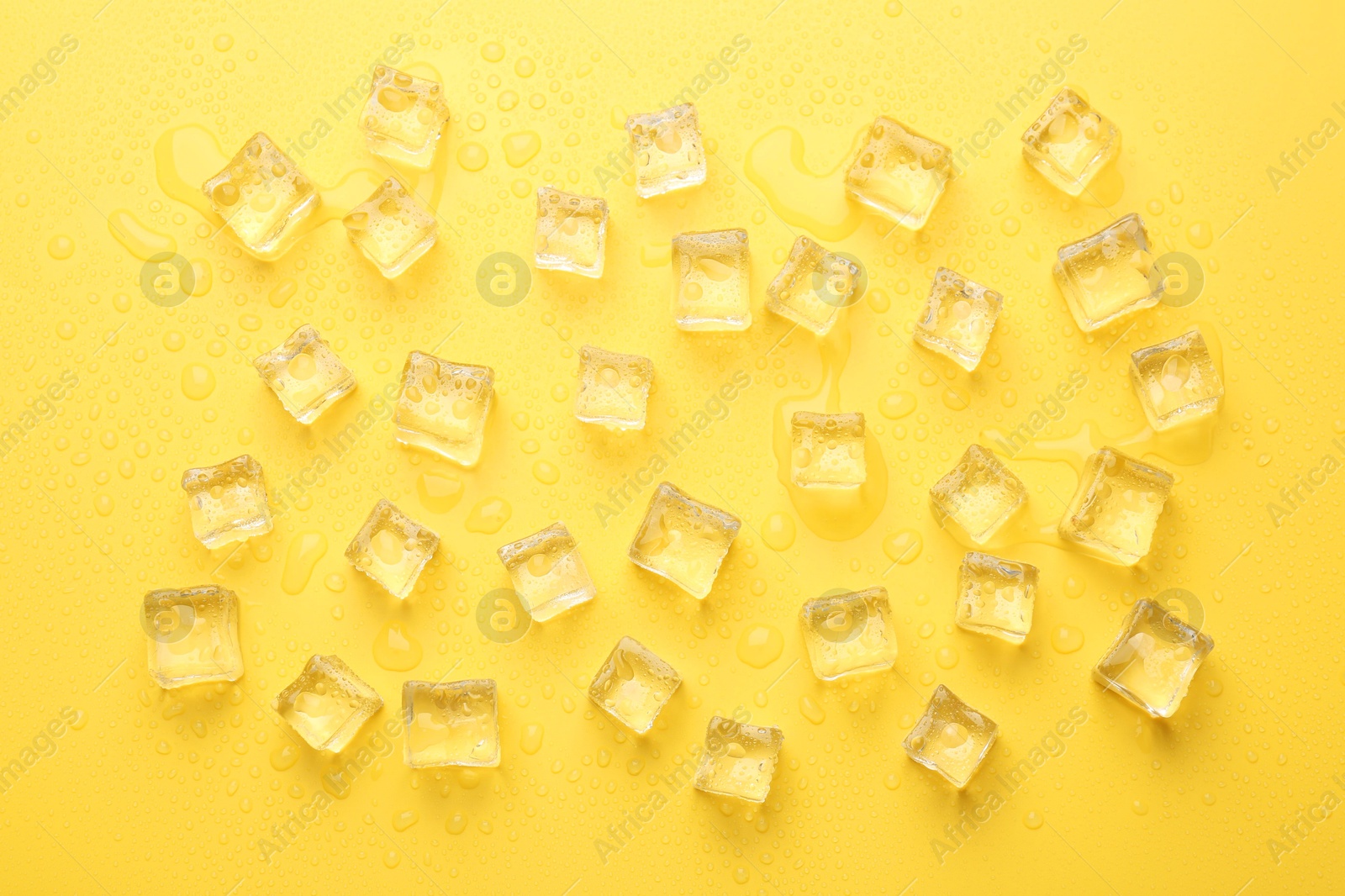 Photo of Crystal clear ice cubes on yellow background, flat lay