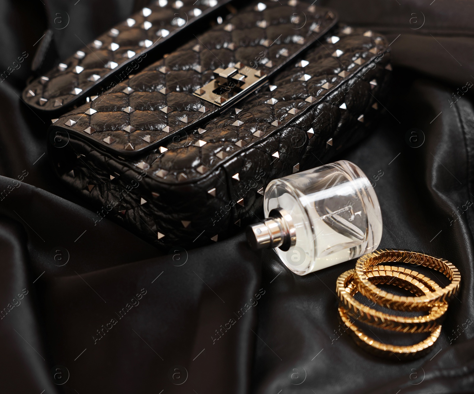 Photo of Leather bag, bottle of perfume and golden bracelets on black fabric, closeup. Space for text