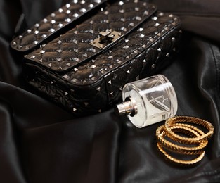 Photo of Leather bag, bottle of perfume and golden bracelets on black fabric, closeup. Space for text