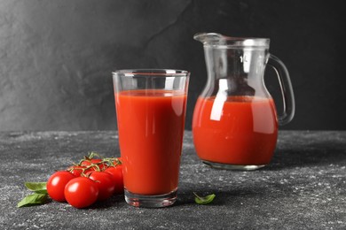 Tasty tomato juice in glass, jug, basil and fresh vegetables on grey table