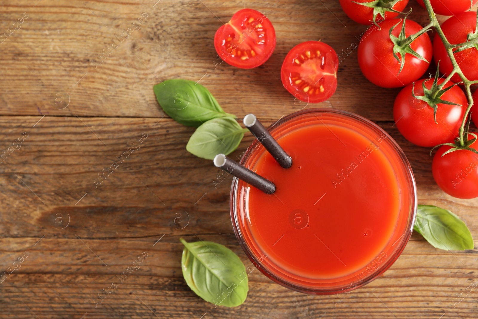 Photo of Tasty tomato juice in glass, basil leaves and fresh vegetables on wooden table, flat lay. Space for text