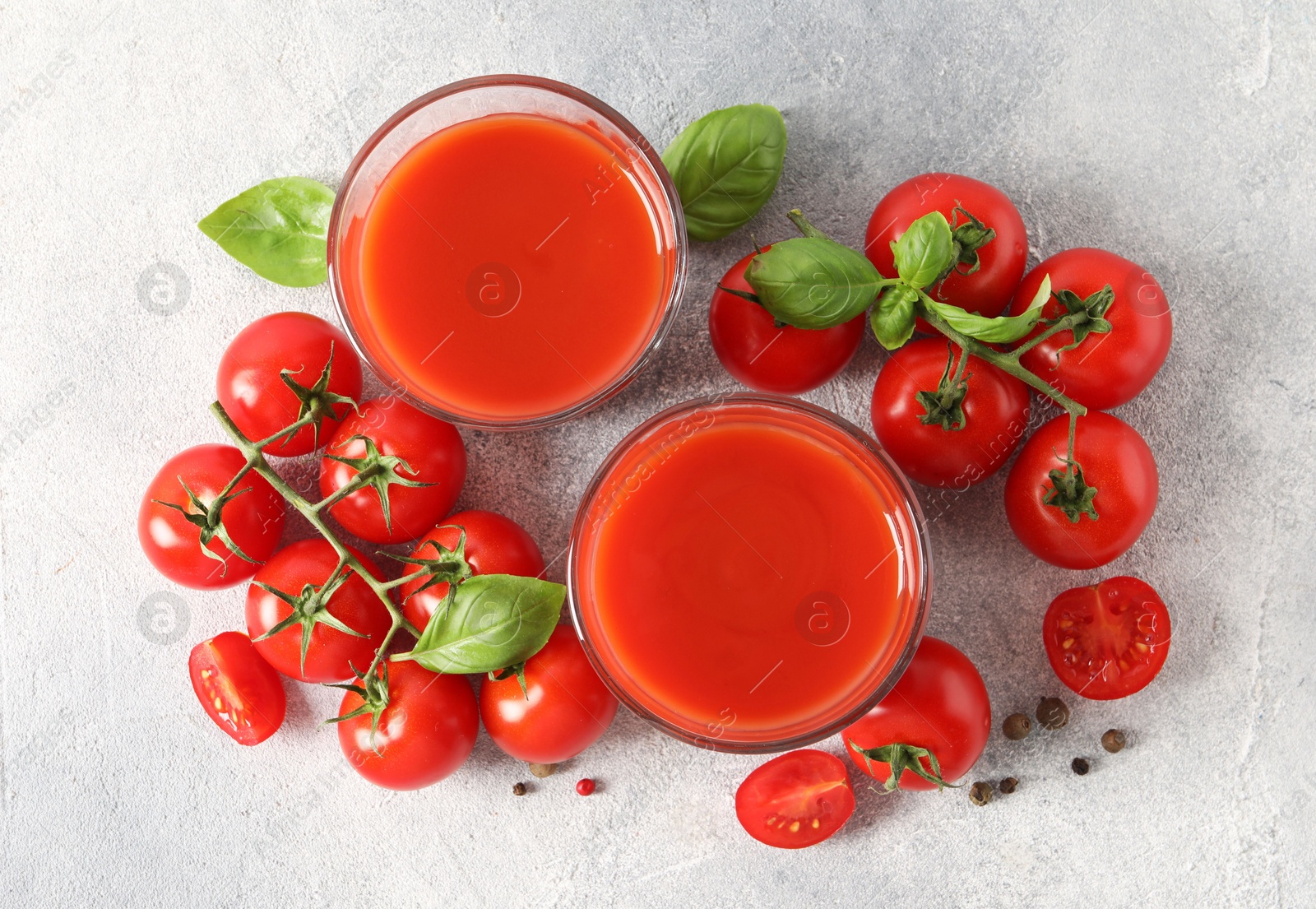 Photo of Tasty tomato juice in glasses, basil leaves, fresh vegetables and peppercorns on light grey table, flat lay