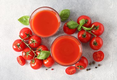 Photo of Tasty tomato juice in glasses, basil leaves, fresh vegetables and peppercorns on light grey table, flat lay