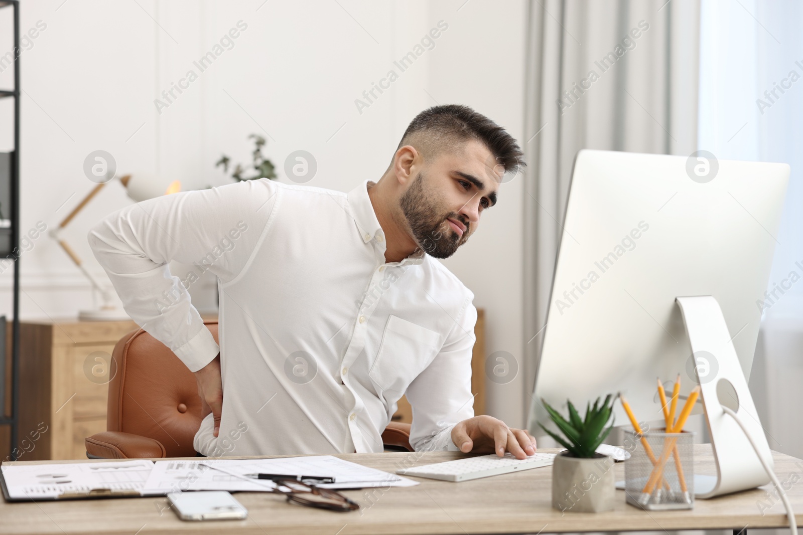 Photo of Man suffering from back pain in office. Symptom of poor posture